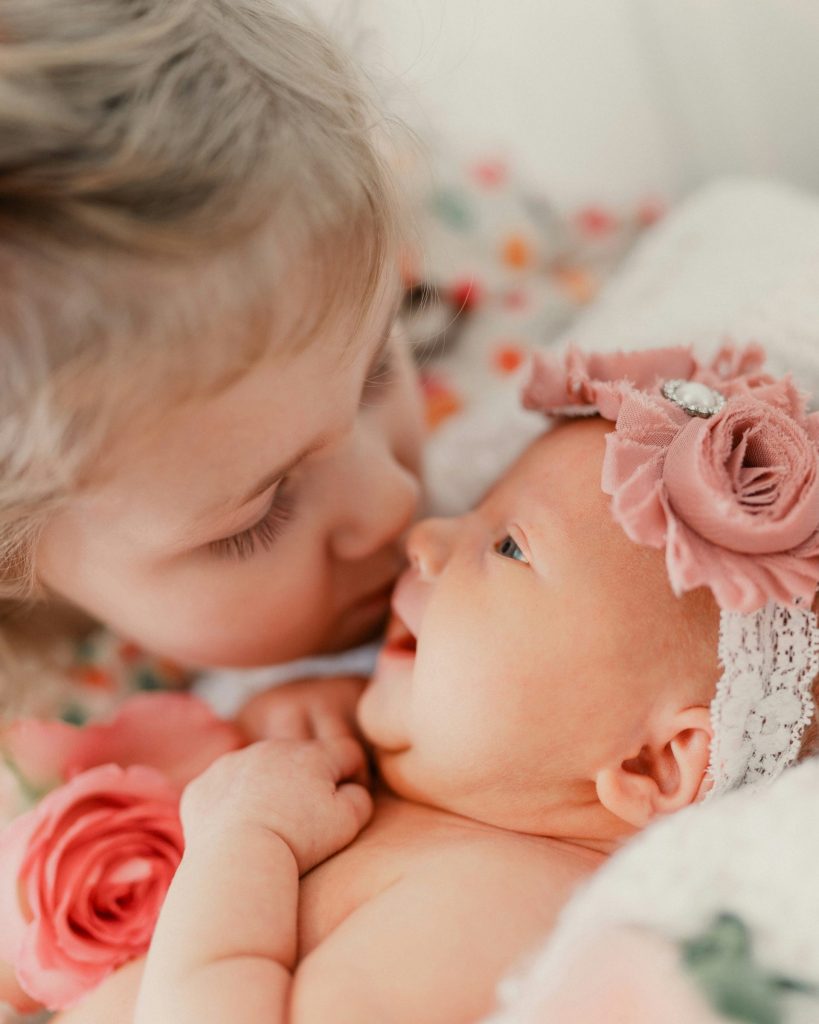 Big sister gently kisses newborn baby sister
